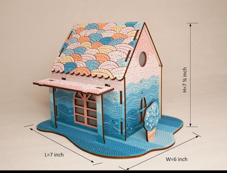 May include: A wooden 3D model of a house with a blue and pink paint scheme. The roof is decorated with a pattern of overlapping scales. The house is 7 1/4 inches tall, 7 inches long, and 6 inches wide.