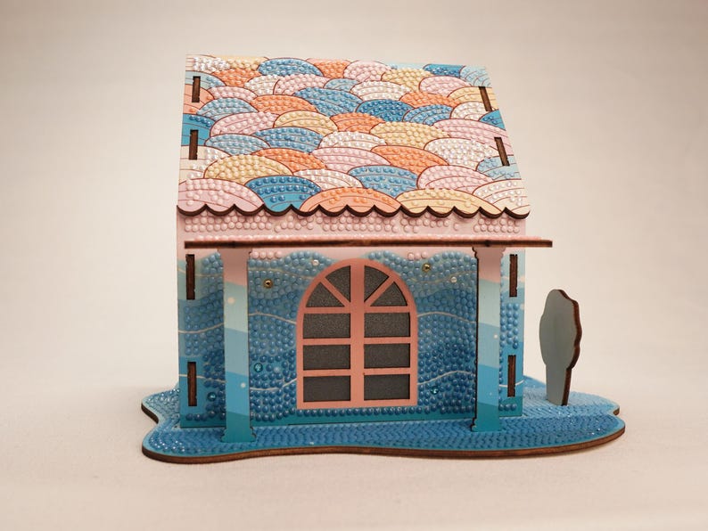 May include: A small wooden house with a pink roof and blue walls. The roof is decorated with a pattern of colorful waves. The house has a single window with a pink frame and a blue door. The house is sitting on a blue base.