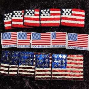 May include: A collection of American flag patches, some with a red, white, and blue embroidered design and others with a sequined design. The patches have the text "God Bless U.S.A." printed on them.