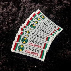 May include: Eight white fabric labels with red, green, and yellow trim. Each label features a black and yellow logo with a green circle and the text "CROSS COLOURS".