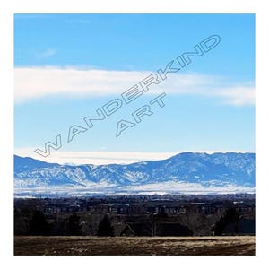 May include: A panoramic view of a snow-capped mountain range in the distance, with a suburban neighbourhood in the foreground. The sky is a bright blue with a few white clouds.