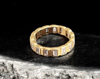 May include: A gold band ring with a row of rectangular clear stones.