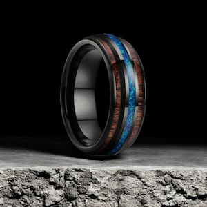 May include: Black tungsten carbide ring with a brown wood inlay and a blue opal inlay.