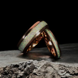 May include: Two rose gold wedding bands with a white opal inlay. The bands are stacked on top of each other.