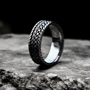 May include: A silver ring with a textured, braided design. The ring is made of metal and has a polished finish.