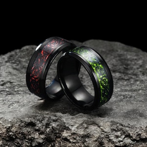 Könnte beinhalten: Zwei schwarze Ringe mit einem keltischen Knotendesign. Ein Ring hat eine rote Einlage und der andere eine grüne Einlage.