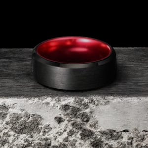 May include: A black tungsten carbide ring with a red interior. The ring has a brushed finish.