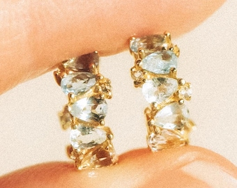 May include: A pair of gold hoop earrings with a row of clear faceted stones.
