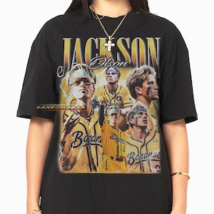 Peut inclure: T-shirt noir avec un graphisme de style vintage représentant un joueur de baseball nommé "Jackson Olson" en lettres dorées. Le design comprend plusieurs images du joueur et le mot "Bananas".