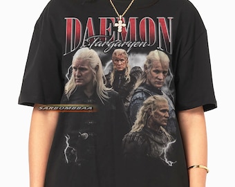 May include: Black t-shirt featuring a graphic of a character with long blonde hair and the text "DAEMON Targaryen" in red and white. The shirt has a vintage, distressed design, with multiple images of the character. The brand name "SARBOMBBAA" is printed on the shirt.