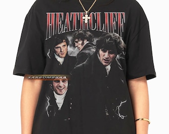 May include: Black t-shirt featuring the name "HEATHCLIFF" in red and white block letters above a collage of images of a man. The shirt has a vintage, distressed look.