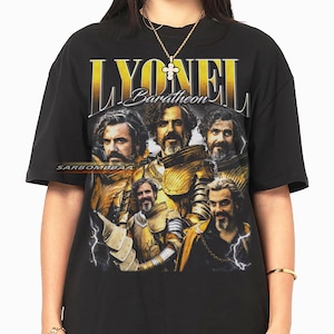 May include: Black t-shirt featuring a graphic of a man in golden armor with the name "LYONEL Baratheon" in gold lettering. The design includes multiple images of the same man. The shirt has a crew neck and short sleeves.