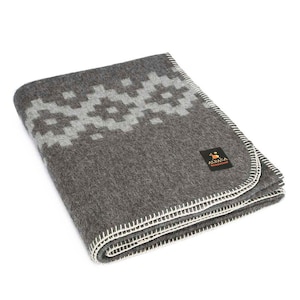 May include: A grey alpaca wool throw blanket with a white geometric pattern border. The blanket is folded and has a white stitched edge. The blanket has a small label that says "Alpaca Warehouse".
