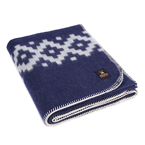 Peut inclure: Une couverture en laine d'alpaga bleu marine avec un motif géométrique blanc. La couverture est pliée et a une bordure blanche cousue. La couverture porte une petite étiquette indiquant "Alpaca Warehouse".