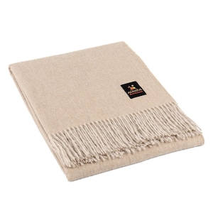 May include: A beige alpaca throw blanket with a fringe border. The blanket has a small label that says "Alpaca Warehouse".