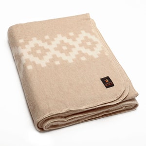 May include: A beige alpaca wool throw blanket with a white geometric pattern and a small brown label that says "Alpaca Warehouse".