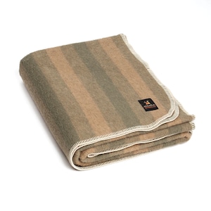 Peut inclure: Une couverture en laine d'alpaga rayée pliée avec une bordure crème. La couverture a un motif rayé brun et vert. La couverture porte une petite étiquette indiquant "Alpaca Warehouse".