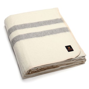 May include: A white alpaca wool blanket with two gray stripes. The blanket is folded and has a small label that says "Alpaca Warehouse" in the bottom right corner.