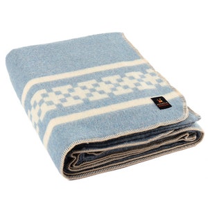 May include: A folded blue and white wool blanket with a checkered pattern. The blanket is made by the company "AACA" and has a cream colored border.