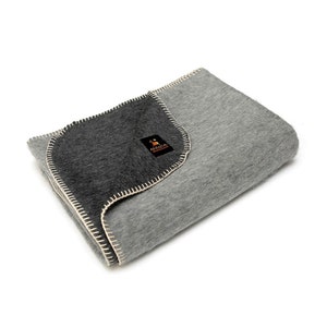 May include: A gray and black alpaca wool throw blanket with a white stitched border. The blanket is folded in half and the label "Alpaca Remarkable" is visible.