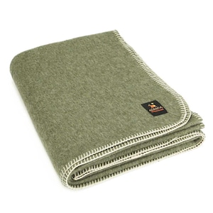 Peut inclure: Une couverture en laine verte avec une bordure blanche cousue. La couverture est pliée et porte une petite étiquette brune avec le texte "Alpaca Warehouse".