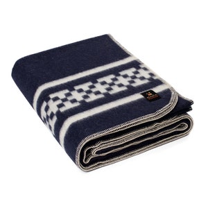 May include: A navy blue wool blanket with a white and black checkered pattern. The blanket is folded and has a small label with the text "AASKA" on it.