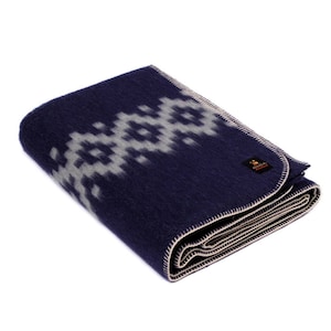 May include: A navy blue wool blanket with a white geometric pattern. The blanket is folded and has a white label with the word "Alpaca" on it.