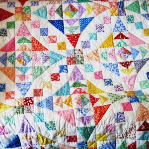 May include: A colorful patchwork quilt with a white background. The quilt features various geometric shapes, including triangles and squares, in a variety of floral and patterned fabrics. The colors include red, pink, blue, yellow, and green.