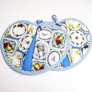 May include: Two round pot holders with a blue and white gingham trim. The fabric features a pattern of plates with fruit, flowers, and bees. Each pot holder has a blue loop for hanging.
