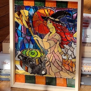 Può includere: Un'opera d'arte in vetro colorato incorniciata raffigurante una strega che mescola un calderone. La strega ha i capelli rossi e indossa un cappello nero. L'opera presenta colori vivaci, tra cui arancione, blu e verde, ed è incorniciata.