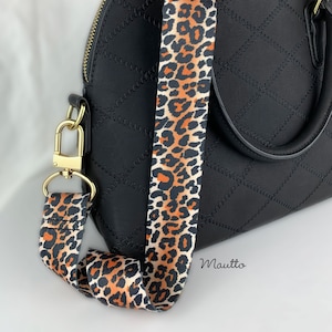 May include: A black quilted handbag with a gold chain and a leopard print adjustable strap. The strap is made of fabric and has a white background with brown and orange leopard spots.