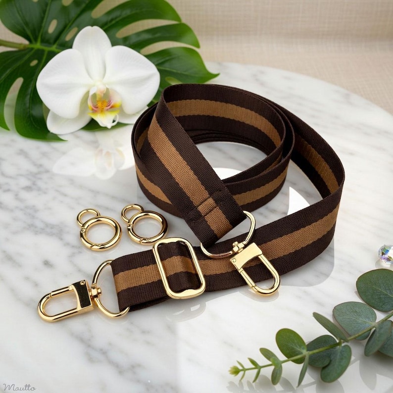 Photo of neverfull tote crossbody strap conversion kit contents in dark brown and golden honey colorway, displayed on a marble surface with flowers/leaves.