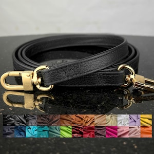 May include: Black leather purse strap with gold-colored metal clasps. The strap is rolled up, showing its length and texture. A color palette of leather swatches is displayed below the strap.
