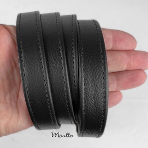 Black pebbled texture leather purse strap held in hand.