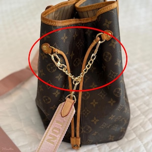 Puede incluir: Bolso de mano marrón y beige con un patrón de logotipo repetido. El bolso presenta correas y detalles dorados, con una correa rosa y blanca que dice "TON". El bolso tiene un cierre de cordón.