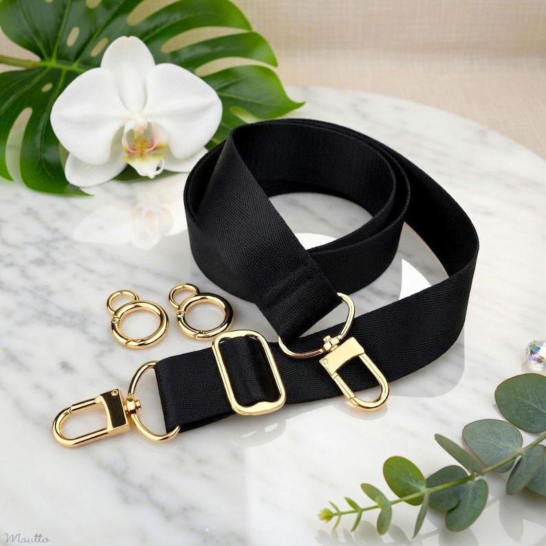 Photo of neverfull tote crossbody strap conversion kit contents in black colorway, displayed on a marble surface with flowers/leaves.