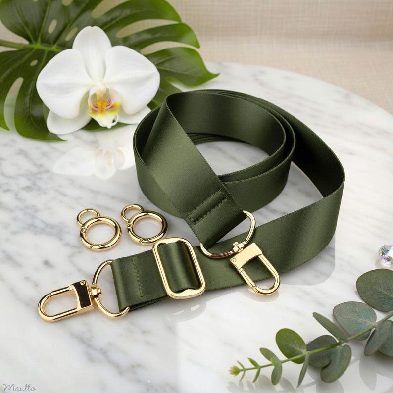 Photo of neverfull tote crossbody strap conversion kit contents in olive colorway, displayed on a marble surface with flowers/leaves.