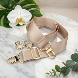 Photo of neverfull tote crossbody strap conversion kit contents in beige colorway, displayed on a marble surface with flowers/leaves.