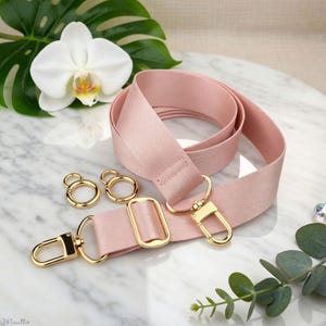Photo of neverfull tote crossbody strap conversion kit contents in pink colorway, displayed on a marble surface with flowers/leaves.