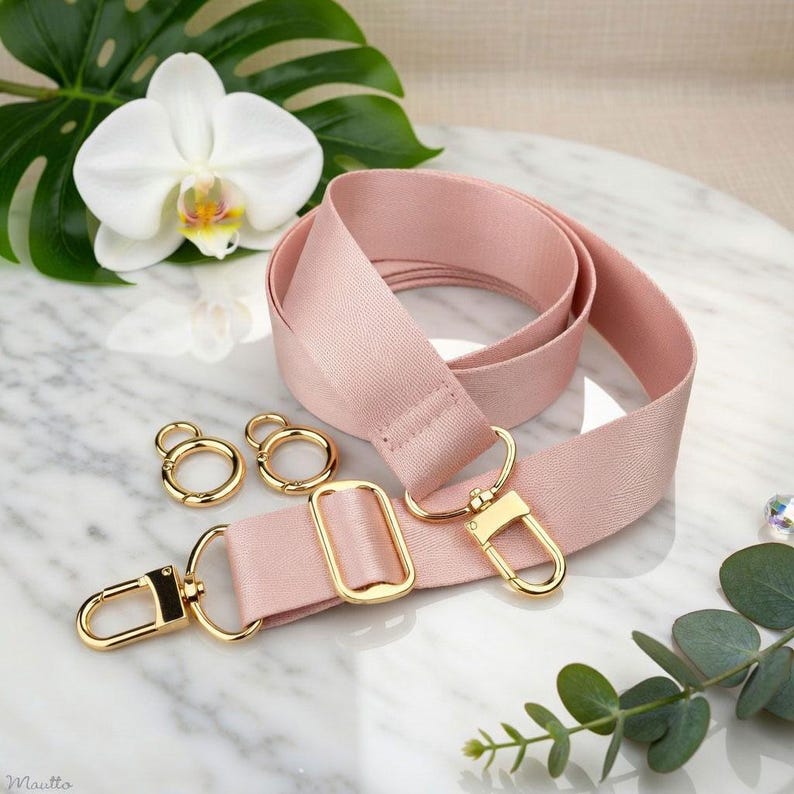 Photo of neverfull tote crossbody strap conversion kit contents in pink colorway, displayed on a marble surface with flowers/leaves.
