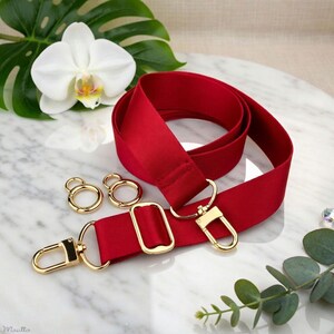 Photo of neverfull tote crossbody strap conversion kit contents in red colorway, displayed on a marble surface with flowers/leaves.
