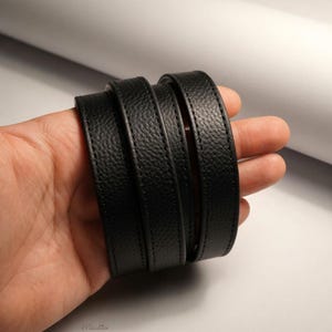 Black pebbled texture leather purse strap held in hand.