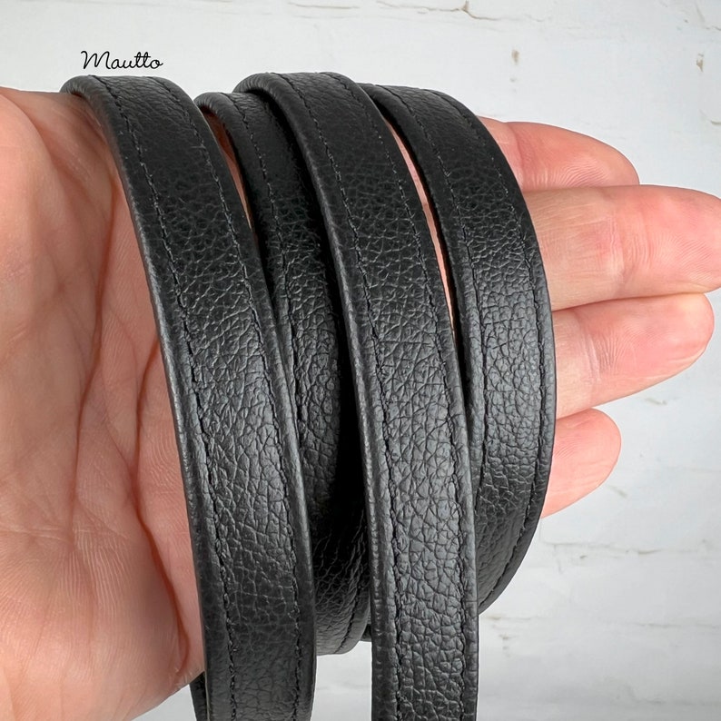 Black pebbled texture leather purse strap held in hand.