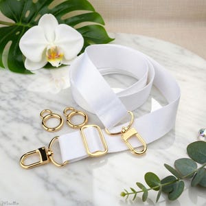 Photo of neverfull tote crossbody strap conversion kit contents in white colorway, displayed on a marble surface with flowers/leaves.