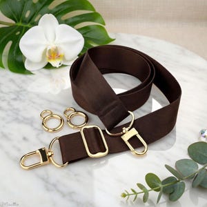 Photo of neverfull tote crossbody strap conversion kit contents in dark brown colorway, displayed on a marble surface with flowers/leaves.