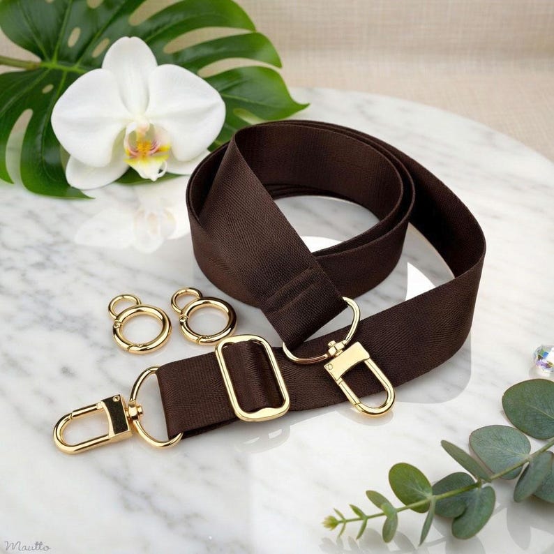 Photo of neverfull tote crossbody strap conversion kit contents in dark brown colorway, displayed on a marble surface with flowers/leaves.