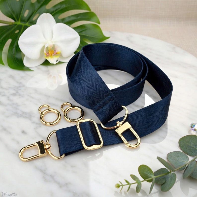 Photo of neverfull tote crossbody strap conversion kit contents in navy colorway, displayed on a marble surface with flowers/leaves.