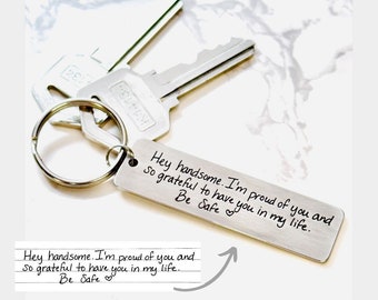 May include: A silver keychain with a small rectangular tag engraved with the message "Hey handsome. I'm proud of you and so grateful to have you in my life. Be Safe."