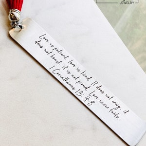 personalized bible verse bookmark featuring engraved scripture and leather tassel displayed beside Bible pages, stainless steel christian bookmark gift with permanent dark laser engraving and brushed silver finish