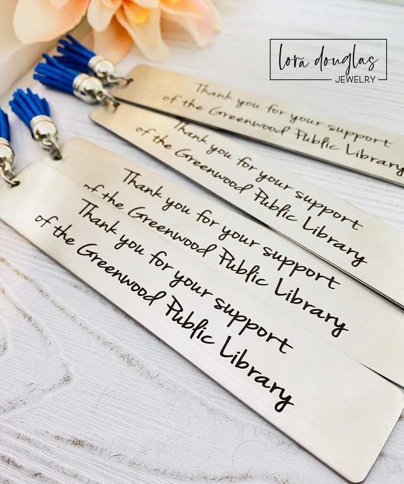 Laser engraved silver stainless steel bookmarks customized with names, quotes, and organization designs. Personalized metal bookmarks with colorful tassels shown styled, highlighting custom font options and meaningful engraving perfect for reading gifts and keepsakes.